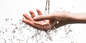 Closeup woman hand under the stream of splashing water - skin care concept